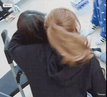 a couple of women are hugging each other in a room . one of the women is wearing a ponytail .