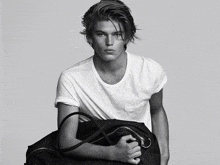 a young man in a white t-shirt holds a black bag