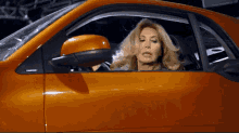 a woman is sitting in an orange car and looking out of the window