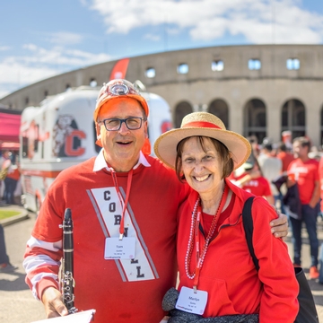 Two Cornell alumni smiling wearing Cornell merch outside of Schoellkopf stadium. 