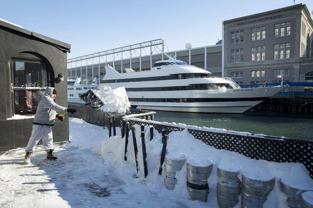 Tossing a shovelful of snow over the railings, Wilson Montano clears a deck at the Whiskey Priest bar on the waterfront. (Robin Lubbock/WBUR)