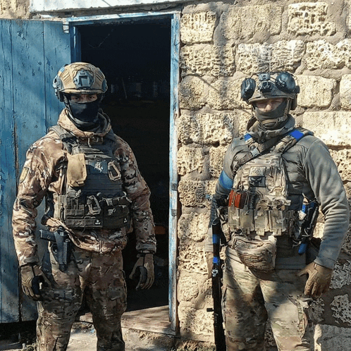 two soldiers are standing in front of a stone building and one of them has the letter a on his chest