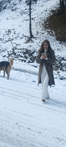 a woman walking down a snowy road with a dog behind her