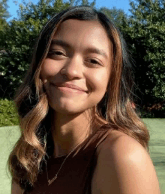 a woman is smiling for the camera while wearing a necklace and a brown tank top .