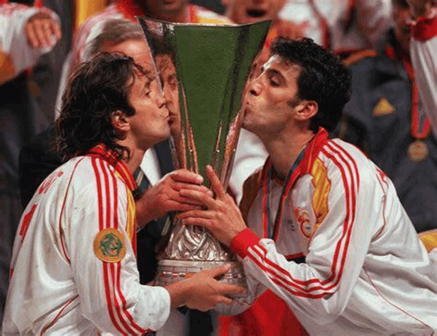 two soccer players are kissing the trophy while holding it in their hands .