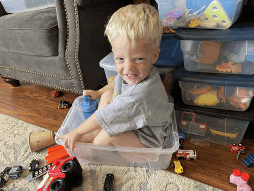 a young boy is sitting in a plastic bin filled with toys