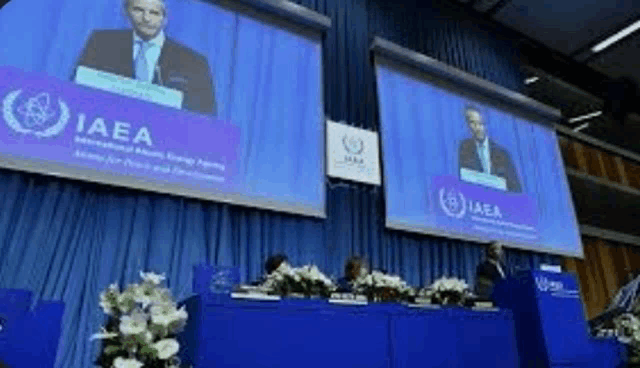 a man in a suit and tie is giving a speech in front of a large screen .