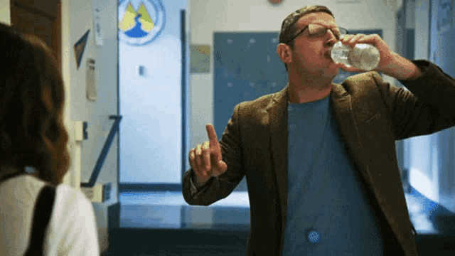 a man drinking water in a hallway with a sign on the wall that says ' a '