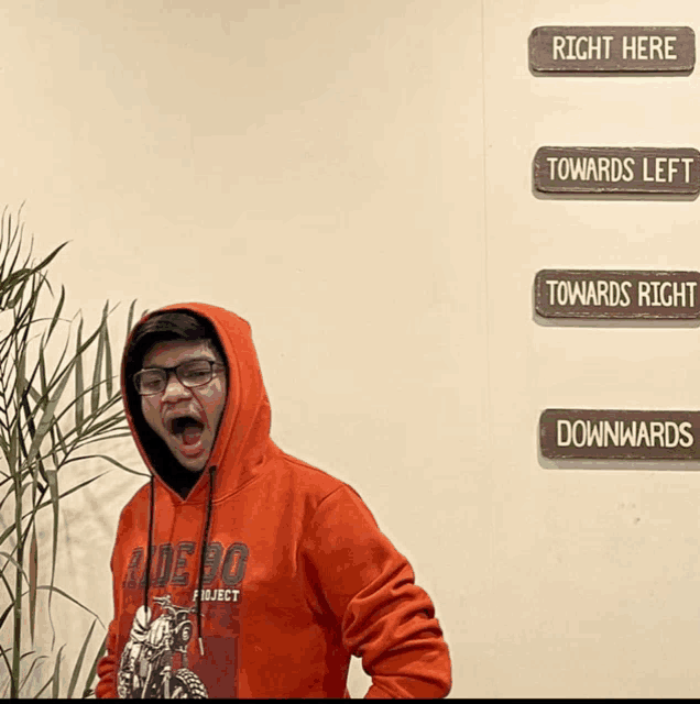 a man wearing a rodeo project hoodie stands in front of a sign that says right here towards left towards right downwards