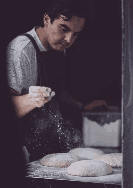 a man in an apron is sprinkling flour on dough on a table