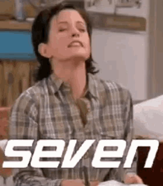 a woman in a plaid shirt is sitting on a couch with her eyes closed and the word seven on the bottom .