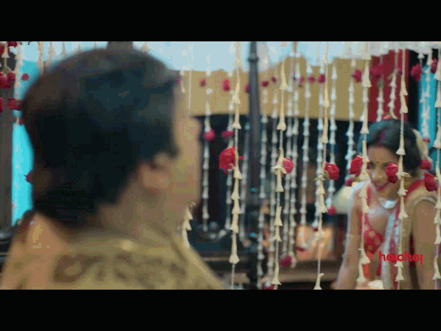 a bride and groom are looking at each other in front of a mirror with flowers hanging from the ceiling