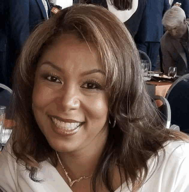 a woman wearing a necklace and earrings smiles for the camera