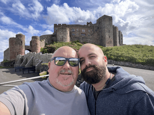 two men pose for a selfie in front of a castle