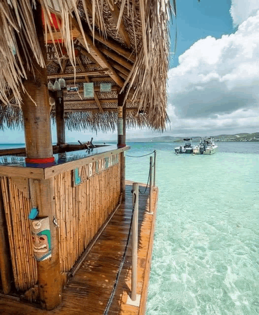 a tiki bar on a dock overlooking the ocean with boats in the distance .