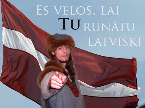 a man pointing in front of a flag with the words es velos lai tu runatu latviski