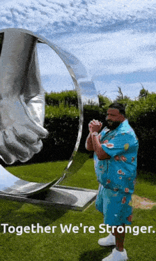 a man in a blue shirt is standing in front of a large sculpture that says together we 're stronger