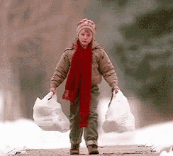 a young boy wearing a red scarf and a hat is walking down a snowy path carrying two plastic bags