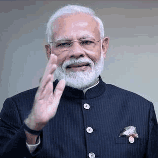 prime minister narendra modi is wearing glasses and a suit and waving his hand .