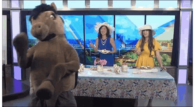 a woman in a yellow dress stands next to a stuffed horse in front of a screen that says good day kentucky