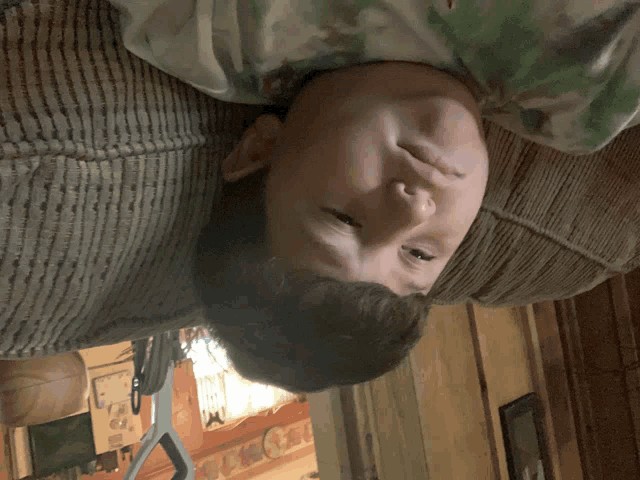 a young boy laying upside down on a couch looking at the camera