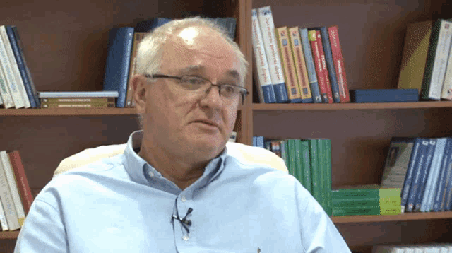 a man wearing glasses sits in front of a bookshelf that has a book titled " a practical guide "