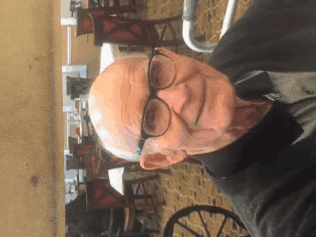 a man wearing glasses and a black jacket stands in front of a restaurant