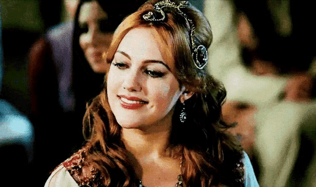 a woman with red hair is wearing a tiara and smiling .