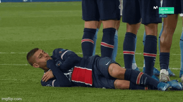 a soccer player is laying on the field with a group of players behind him