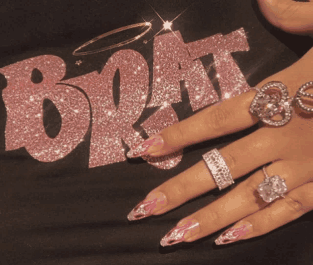 a woman 's hand with many rings and a shirt that says brat