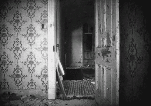 a black and white photo of an old house with a door open and a staircase .