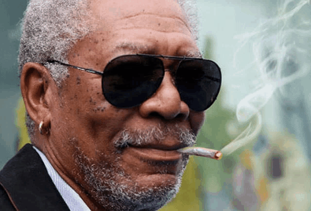 a man wearing sunglasses is smoking a cigarette with smoke coming out of his mouth