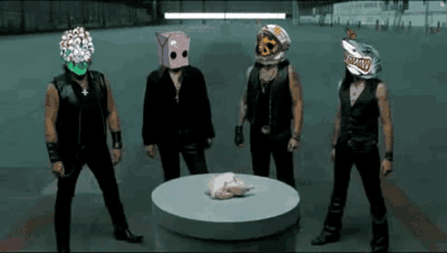 a group of men with masks on their heads are standing around a table with a chicken on it .