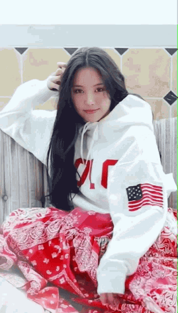 a woman wearing a white hoodie with an american flag on the sleeve is sitting on a couch