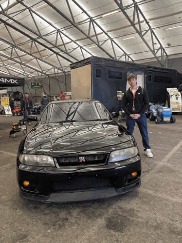 a man stands in front of a black car with a sign that says 4mx