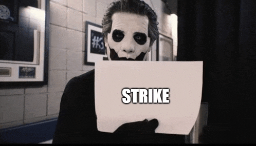 a man in a joker mask holds up a piece of paper that says strike