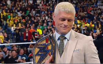 a man in a suit and tie is holding a wrestling championship belt in front of a crowd .