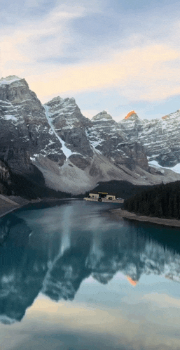 a lake surrounded by snow covered mountains with a house in the middle