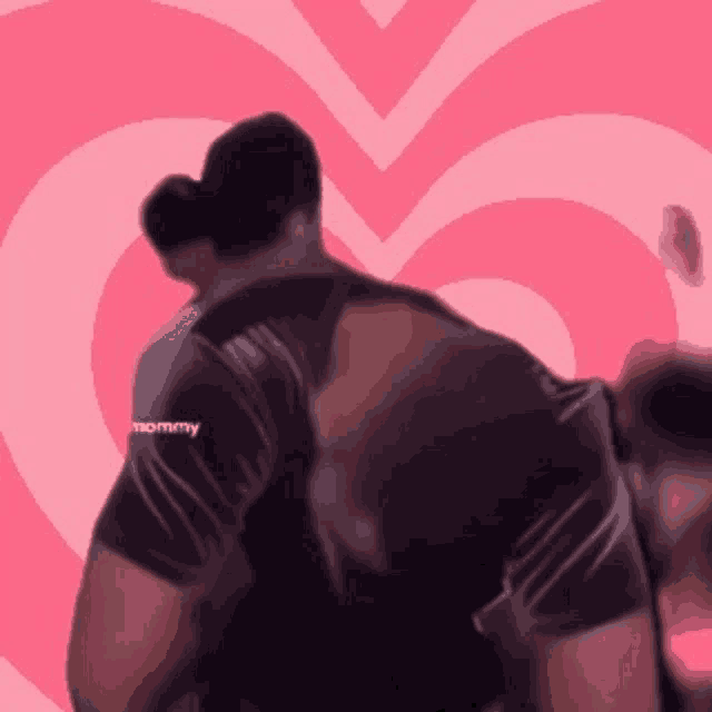 a man in a black shirt is hugging another man in front of a pink heart ..