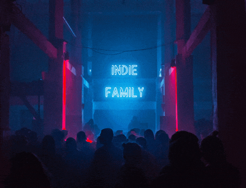 a neon sign that says indie family hangs over a crowd of people