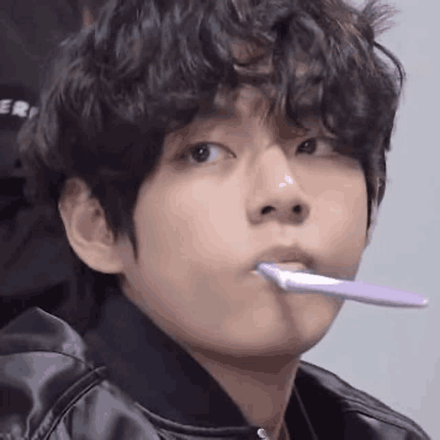 a young man with curly hair is brushing his teeth with a toothbrush .