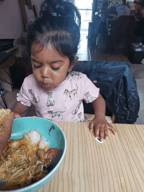 a little girl sitting at a table with a bowl of food on it