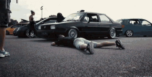 a man is laying on the ground in front of a row of cars with a license plate that says ' a ' on it