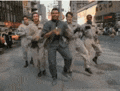 a group of men in suits are walking down a street .