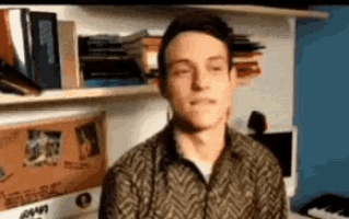 a man with his eyes closed is standing in front of a keyboard and a shelf with books on it .