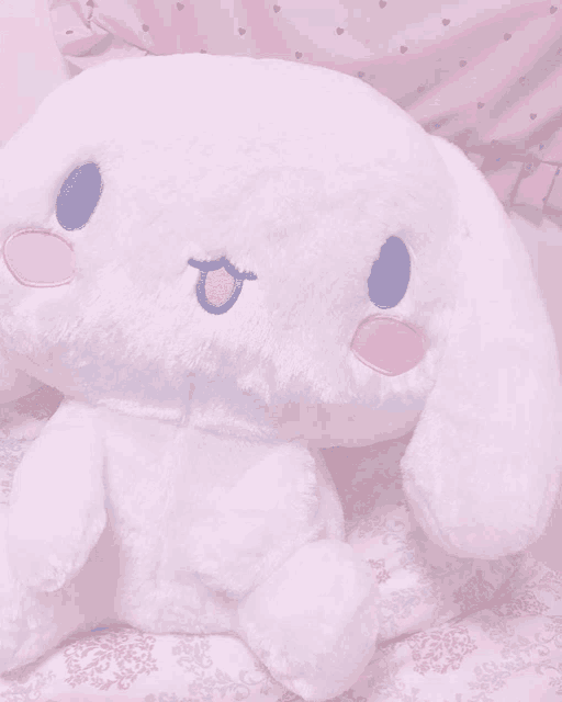 a white stuffed animal with a blue eye is sitting on a bed next to a pink pillow