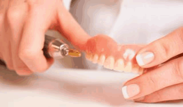 a close up of a person polishing a denture with a machine .