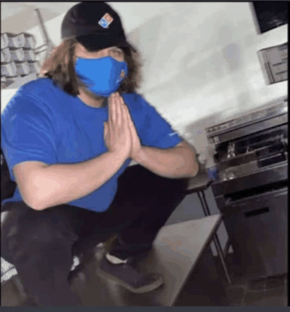 a man wearing a mask and a domino 's hat is squatting down with his hands folded in prayer .