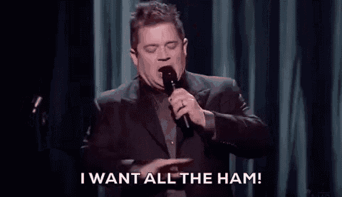 a man in a suit is holding a microphone on a stage and says `` i want all the ham '' .