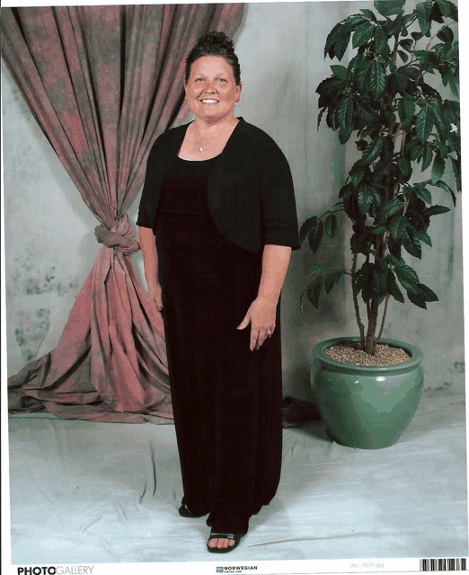 a woman in a black dress is standing next to a potted plant